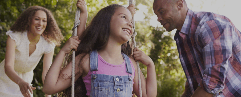young child wearing pink shirt on a swing smiling