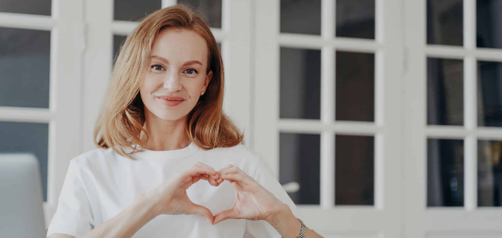 woman wearing white teeshirt making a heart with her hands