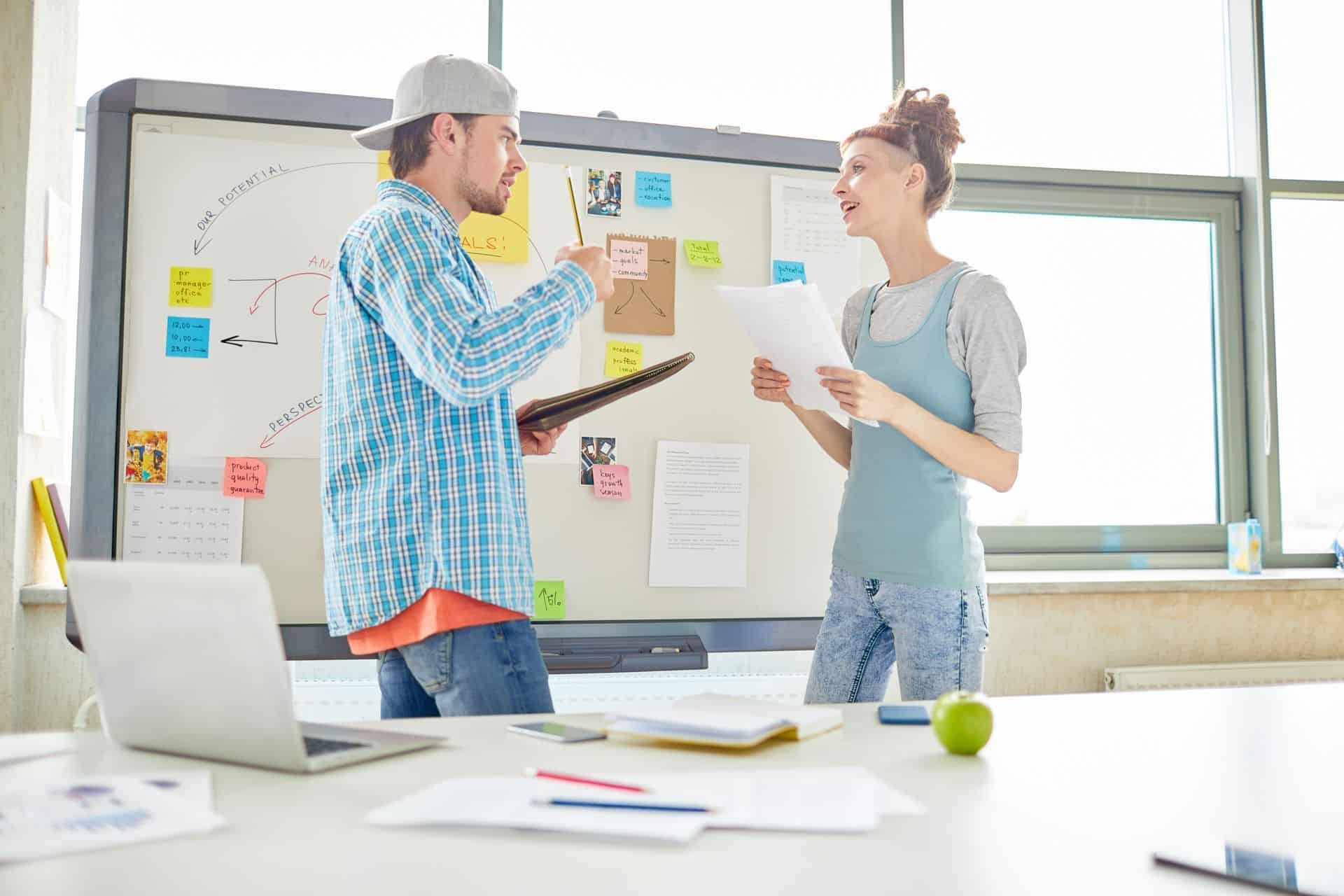 two people talking in front of a white board