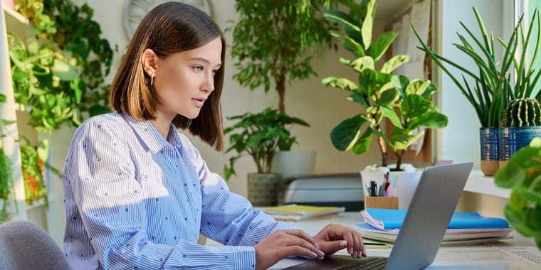 woman wearing blue short working with at computer with green plants in background