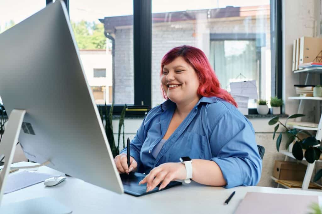 a woman with red hair smiling and working at a desk in an office setting