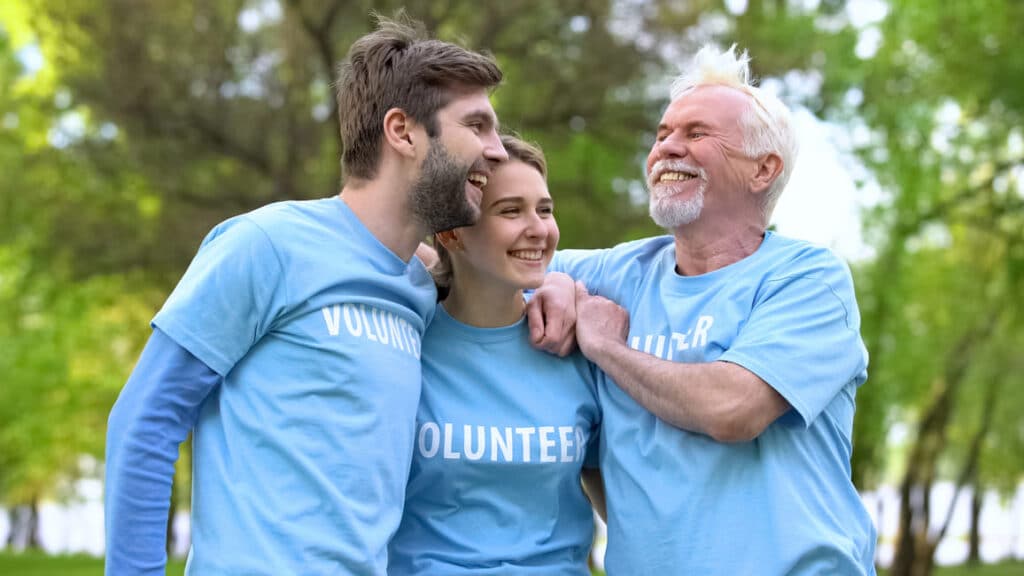 three volunteers of mixed ages wearing light blue tee shirts with the words volunteer across the chest